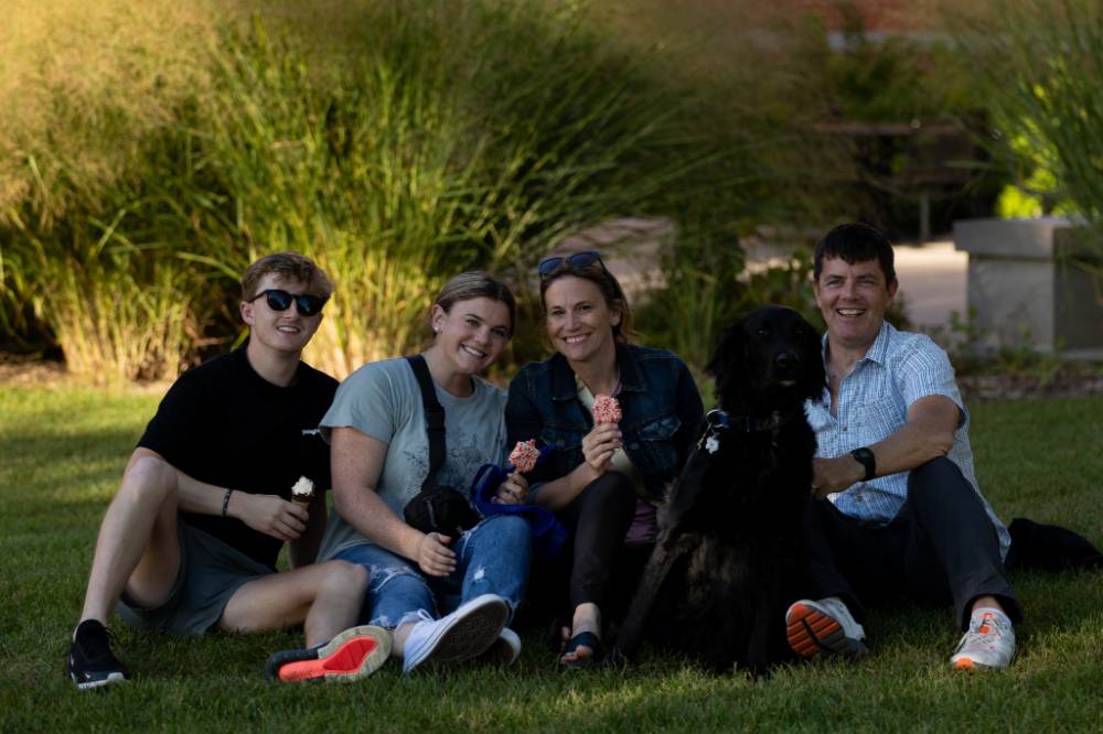 Family posing with dog and ice cream on lawn.
